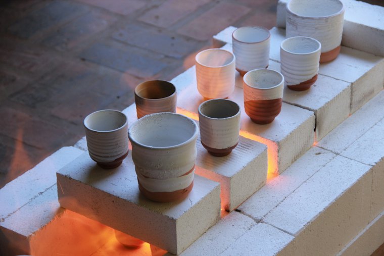 Tasses en grès sorties du four, posées sur des briques.