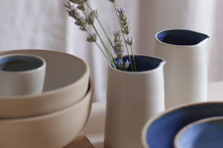 Bols, pichet et vase en grès, posés sur une table claire.